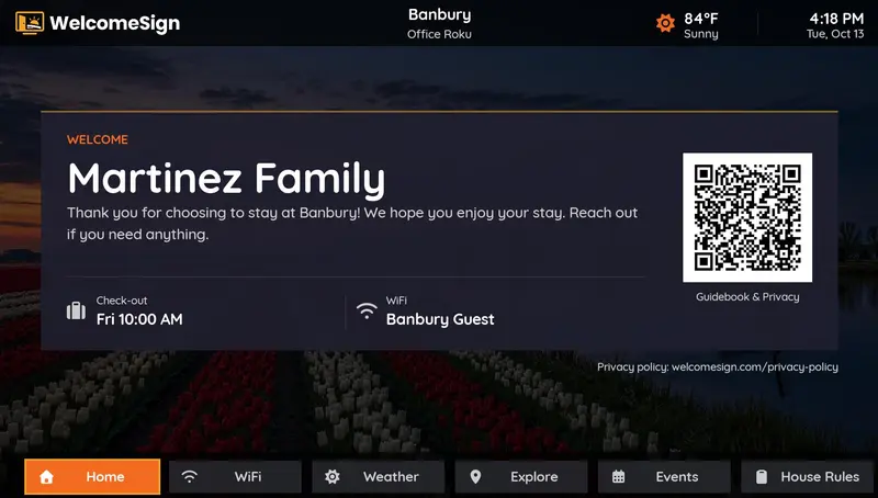 Vacation rental interactive TV display showing a personalized guest greeting, check-out time, local weather, WiFi network, and a guidebook QR code